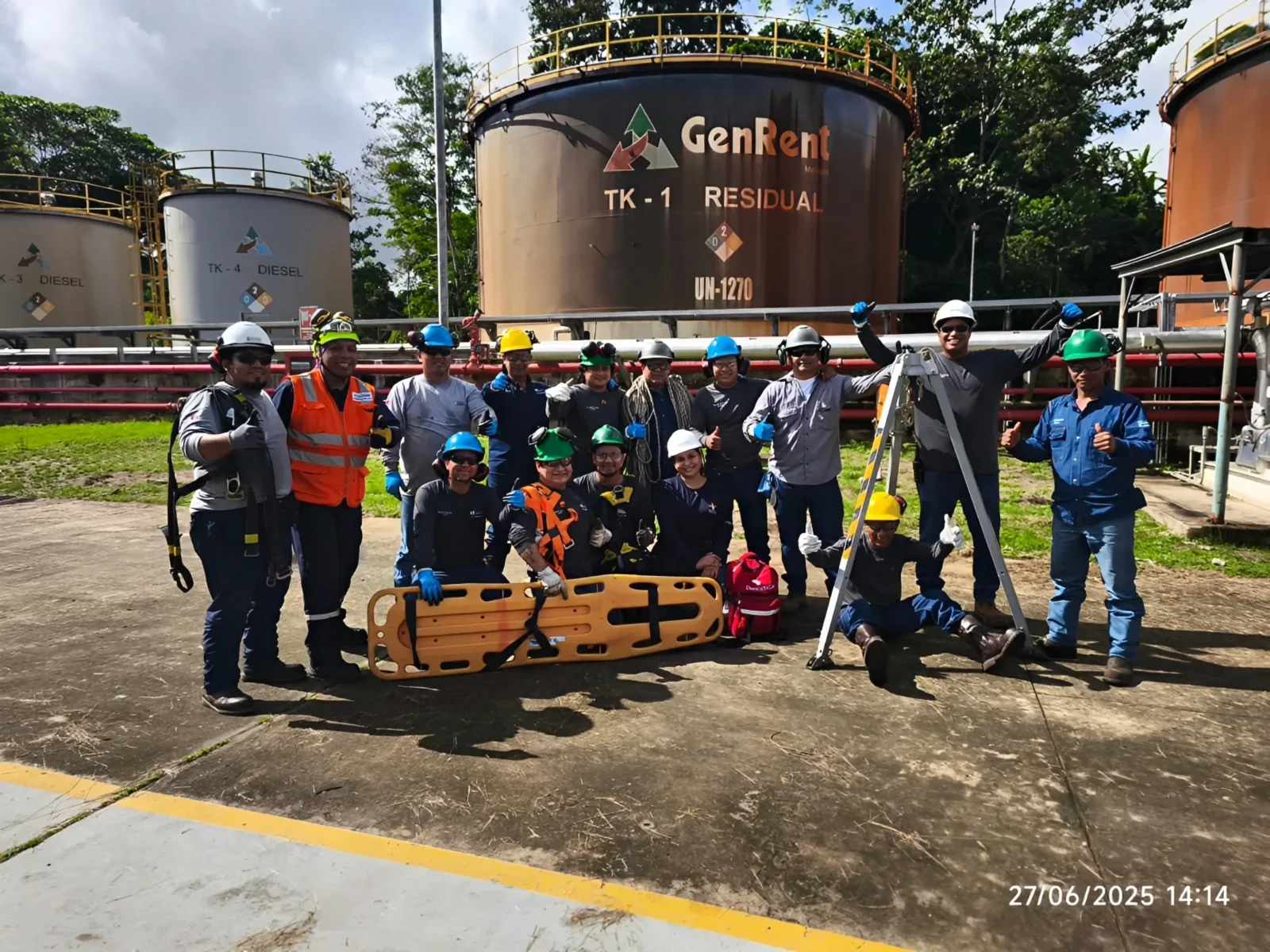 Brigada con cascos y arneses junto a una camilla de rescate frente a los tanques de combustible de una planta