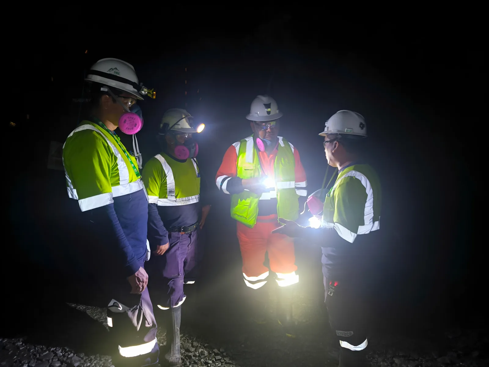 Inspección en interior mina: cuatro trabajadores con respiradores, chalecos reflectivos y linternas
